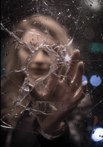 Woman’s face partially reflected through a broken mirror, symbolizing identity diffusion and self-erasure in Emotional Outsourcing™.