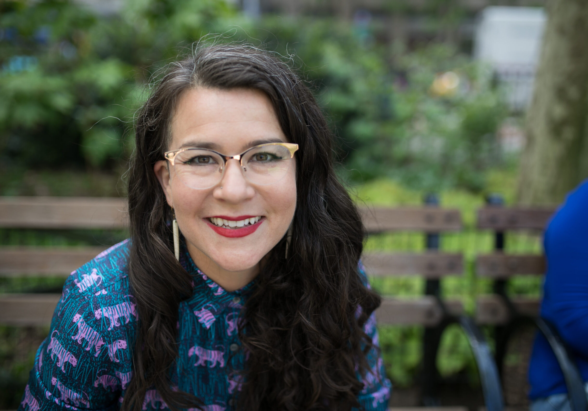 Beatriz Victoria Albina on bench, gold glasses, looking right at camera outside