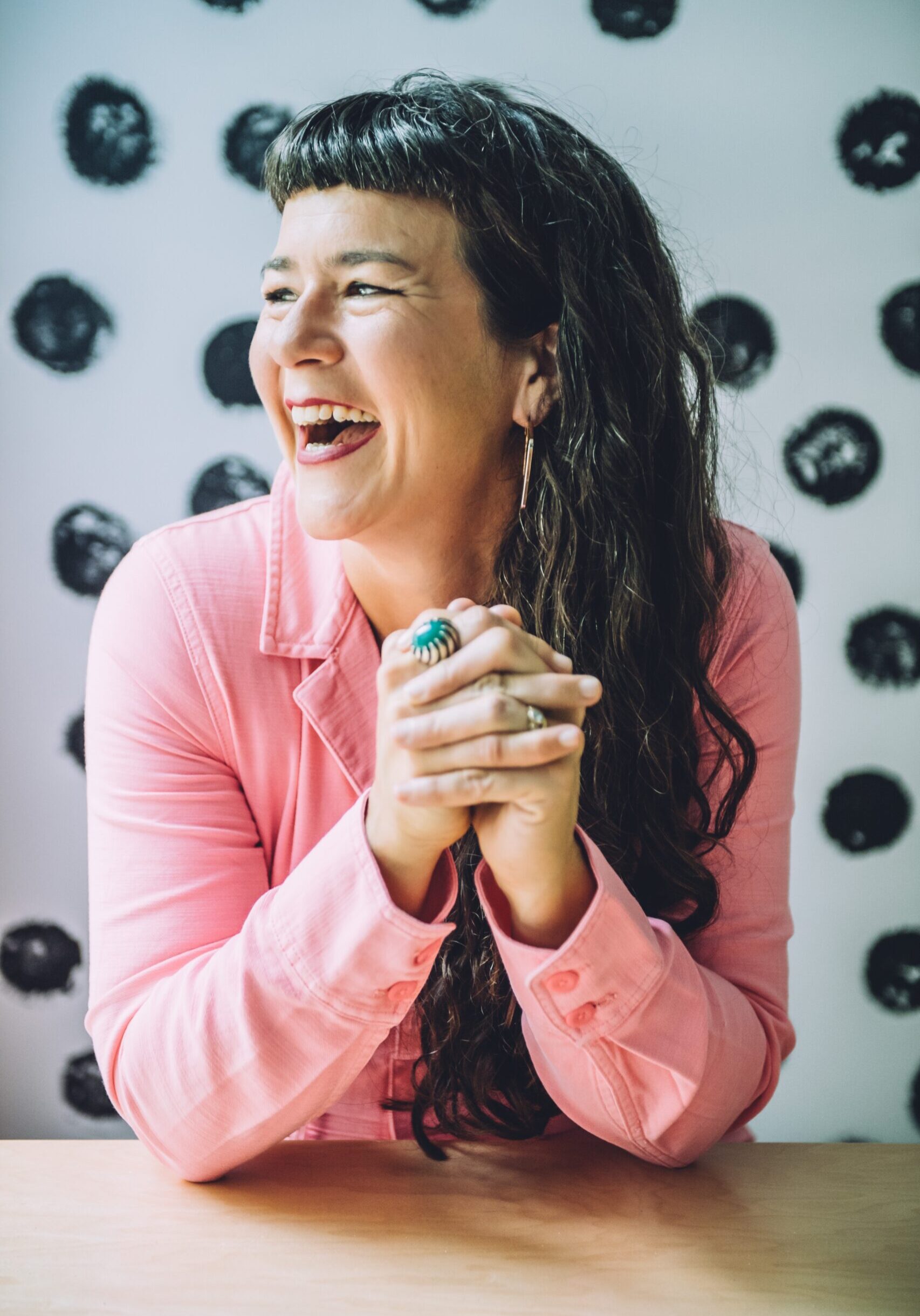 Life coach Victoria Albina in a pink jumpsuit, smiling while sitting at a table